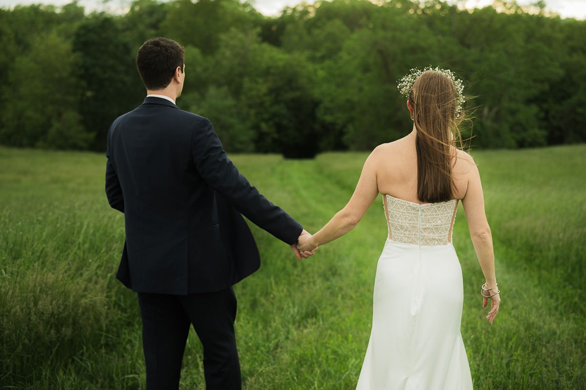 Bride and groom standing looking out into a path in the distance, holding hands. Shady Elm Farms Field in Pittsburgh PA, wedding photography
