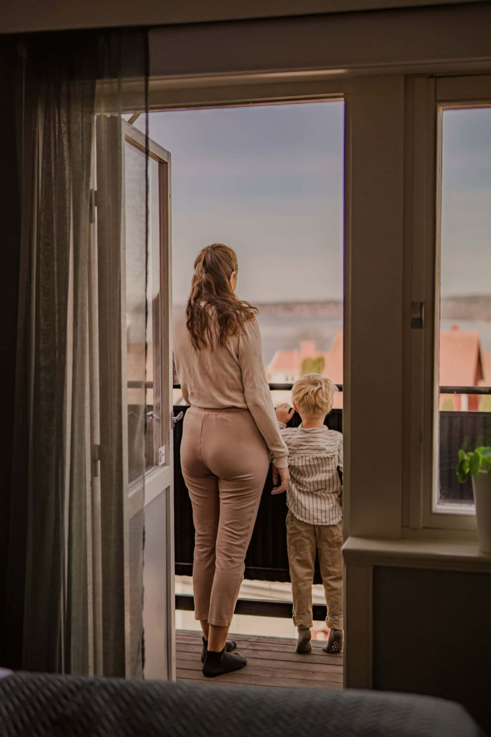 Two people standing on balcony looking at sunset view through open glass doors.