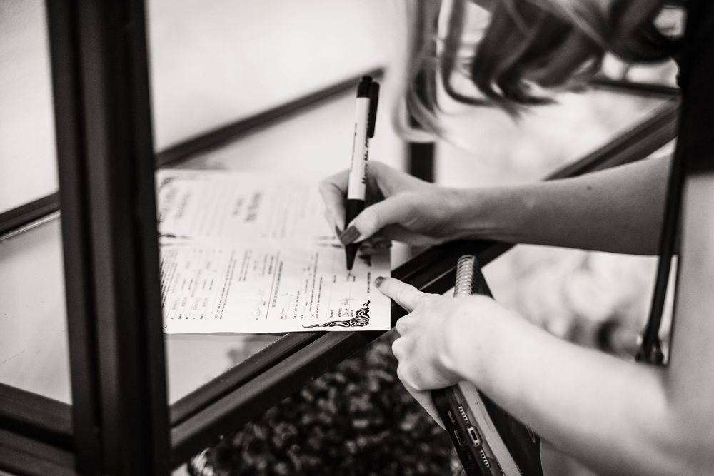 A pair of hands holding a pen while filling out paperwork on a clipboard in black and white.