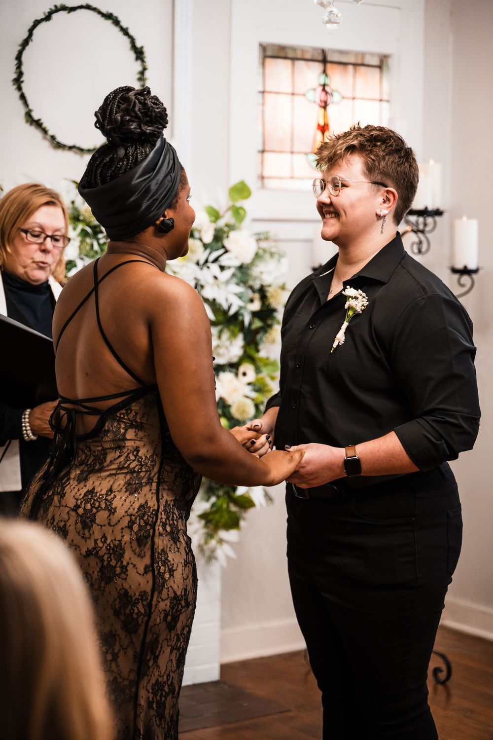 Two people exchange vows during an intimate indoor wedding ceremony surrounded by floral decorations and candlelight.