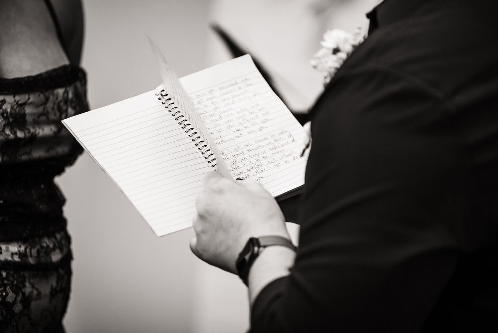 A person holds an open spiral notebook while writing in black and white monochrome photography.