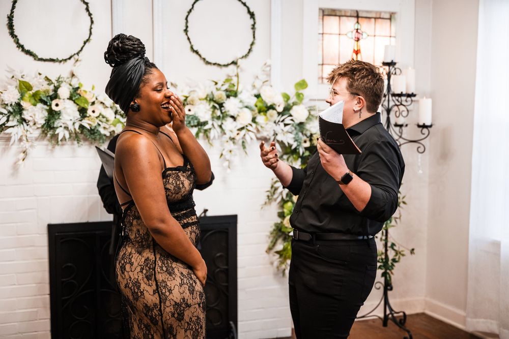 A couple shares an emotional moment during their wedding ceremony in a room decorated with white flowers.