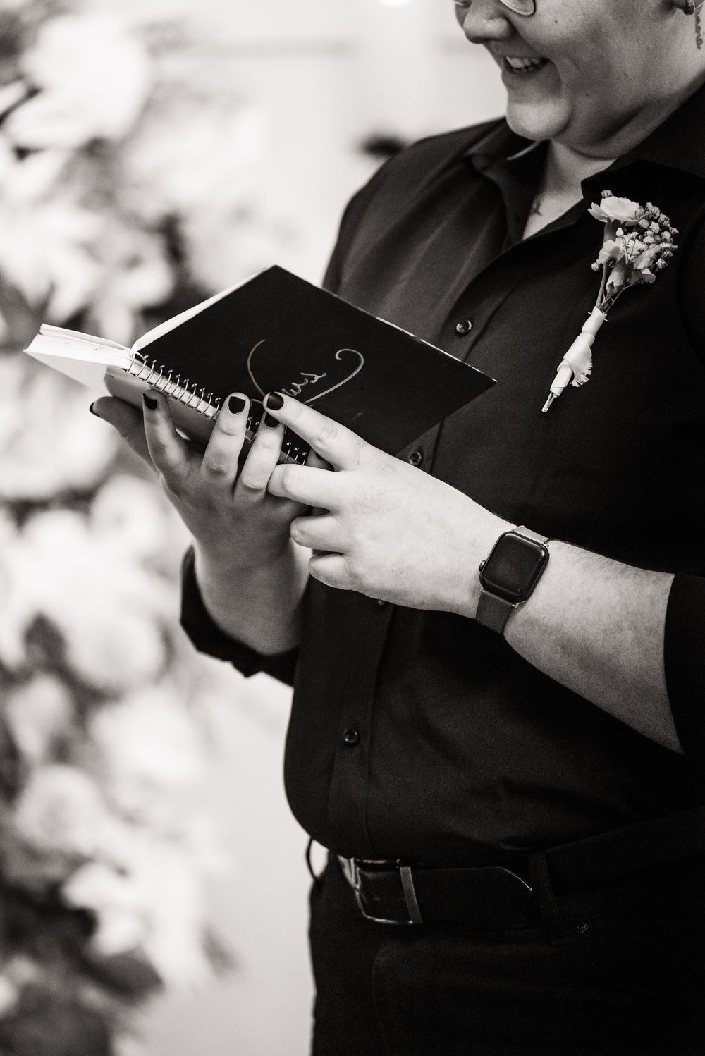 Close-up of hands holding a black notebook during a wedding ceremony with a boutonniere visible.