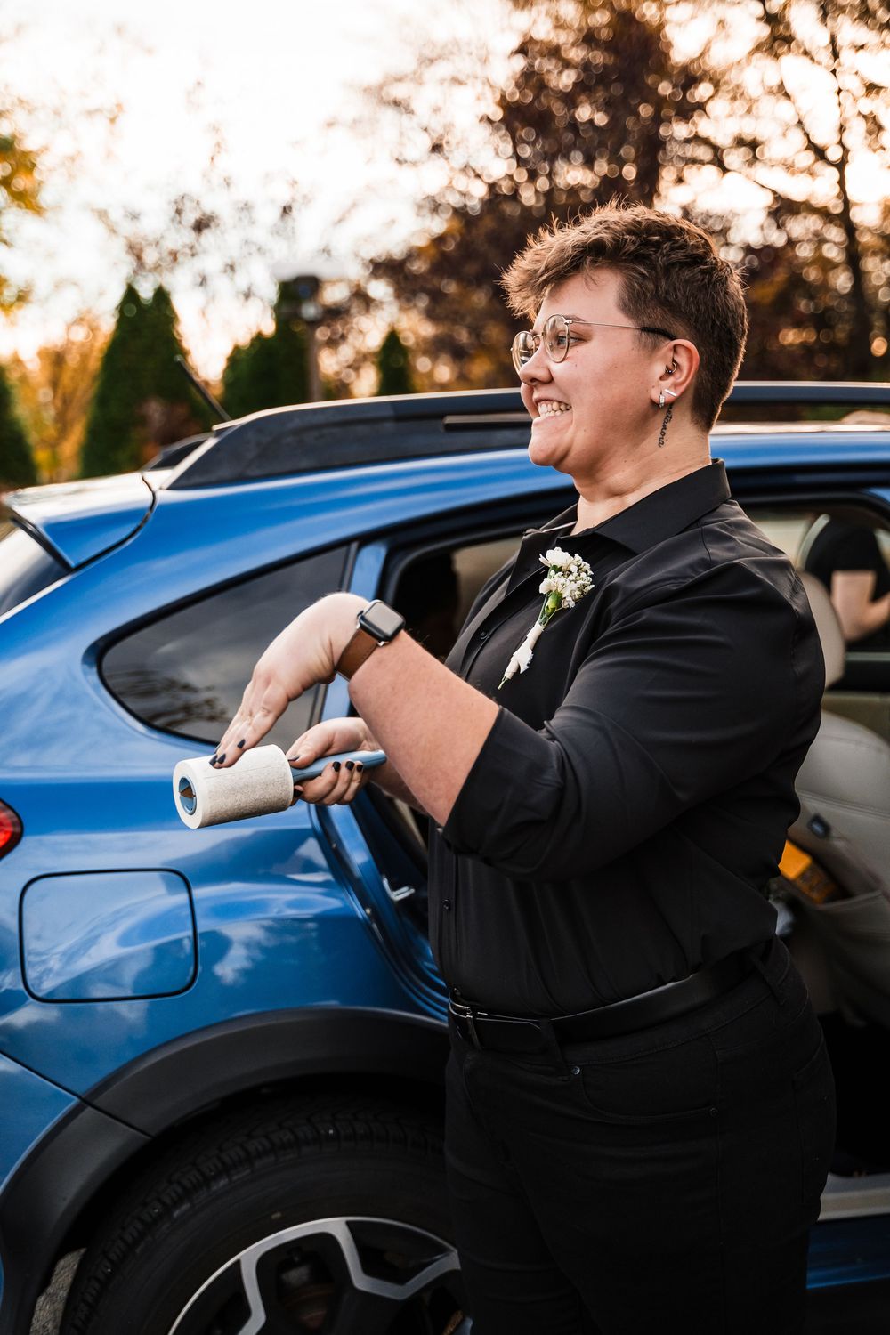 A joyful person in formal black attire charging an electric car at sunset.