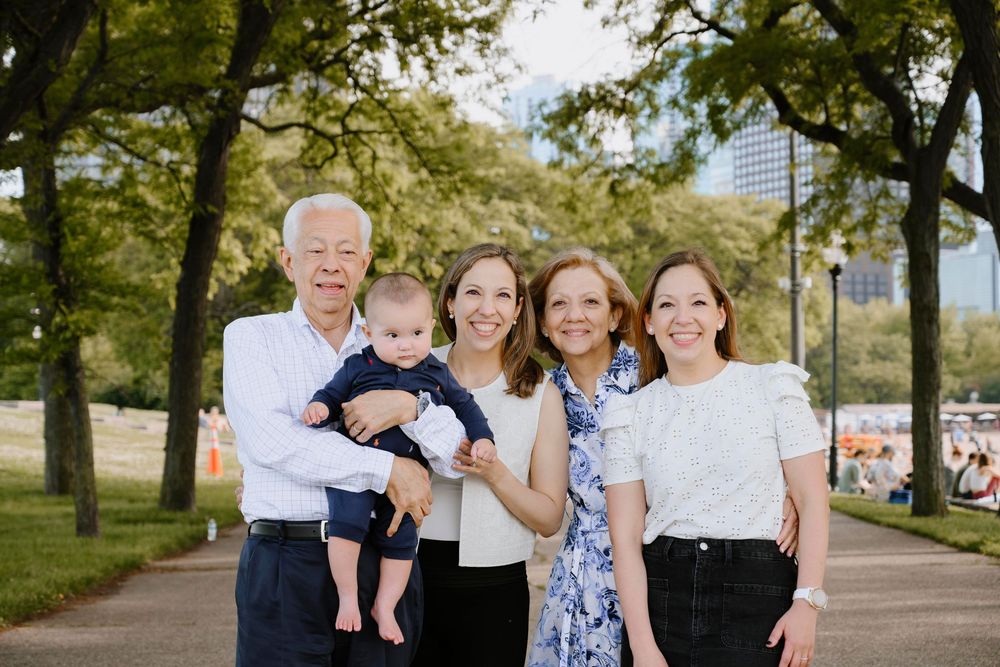 Multi-generational family group poses together on a tree-lined path in a park during summer.