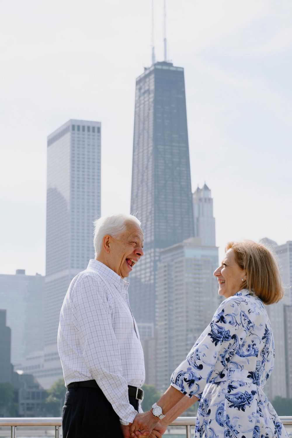 Happy senior couple holding hands and smiling with Chicago skyline and John Hancock building in background.