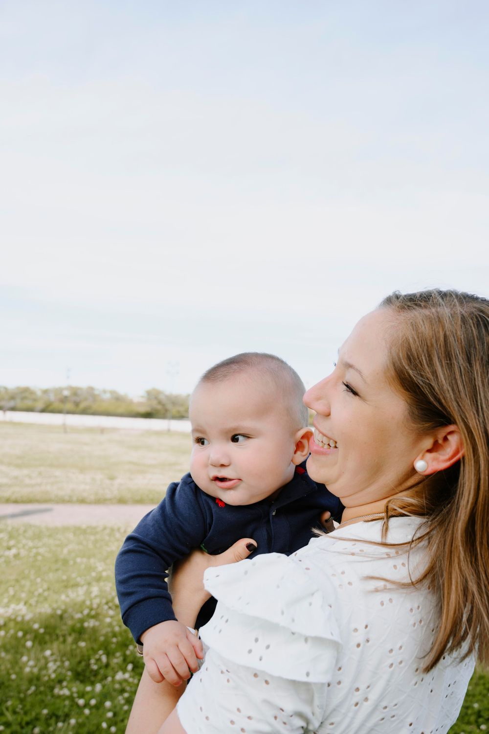 A joyful outdoor moment captured in a grassy field with playful expressions and white eyelet details.