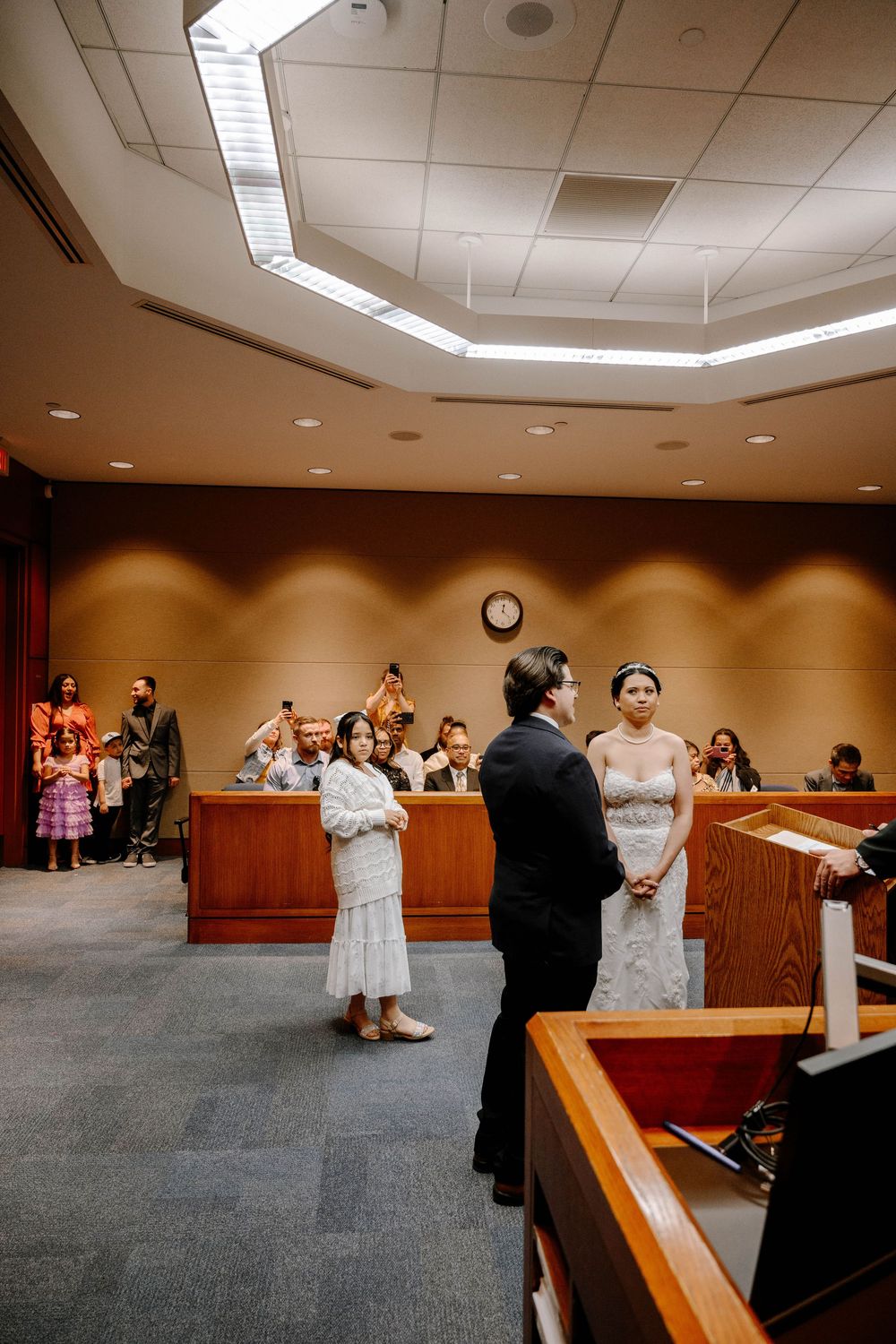Wedding ceremony taking place in a courtroom with attendees seated in viewing gallery.