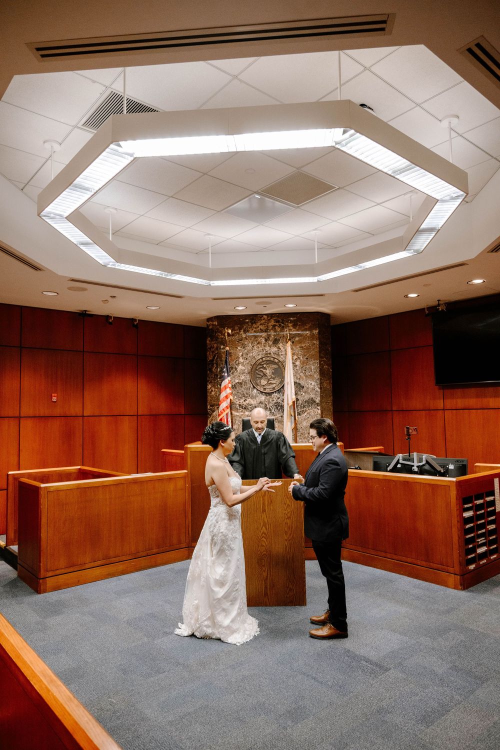 A couple exchanging vows beneath an octagonal skylight in a courthouse ceremony room.