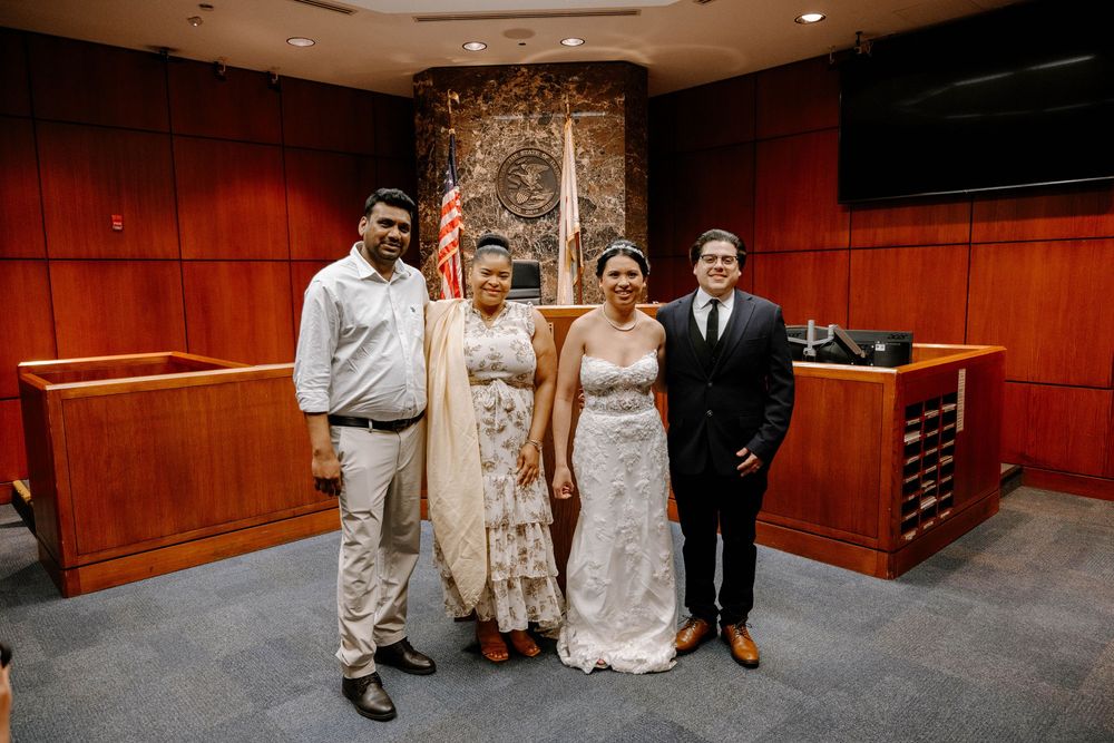 A group of people pose together in a wood-paneled courtroom setting during a wedding ceremony.