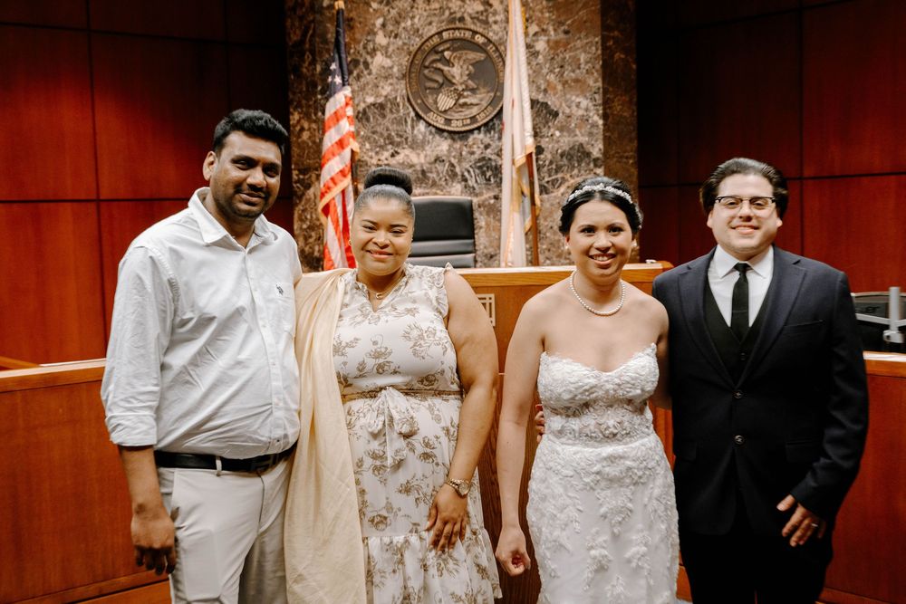 Wedding party of four people smiling and standing together in front of a wooden wall with a seal mounted behind them.