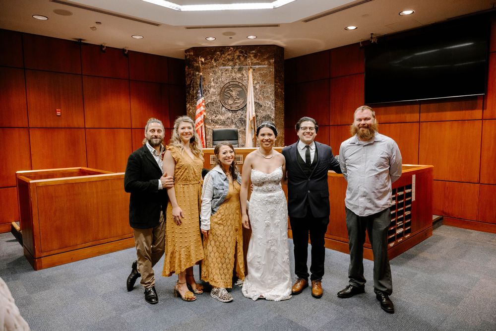 A small group stands together in a wood-paneled courtroom with an American flag and stone wall behind them.