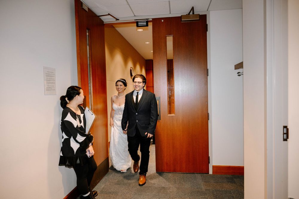 Three people walk and laugh together in a modern office hallway with warm lighting and wood doors.