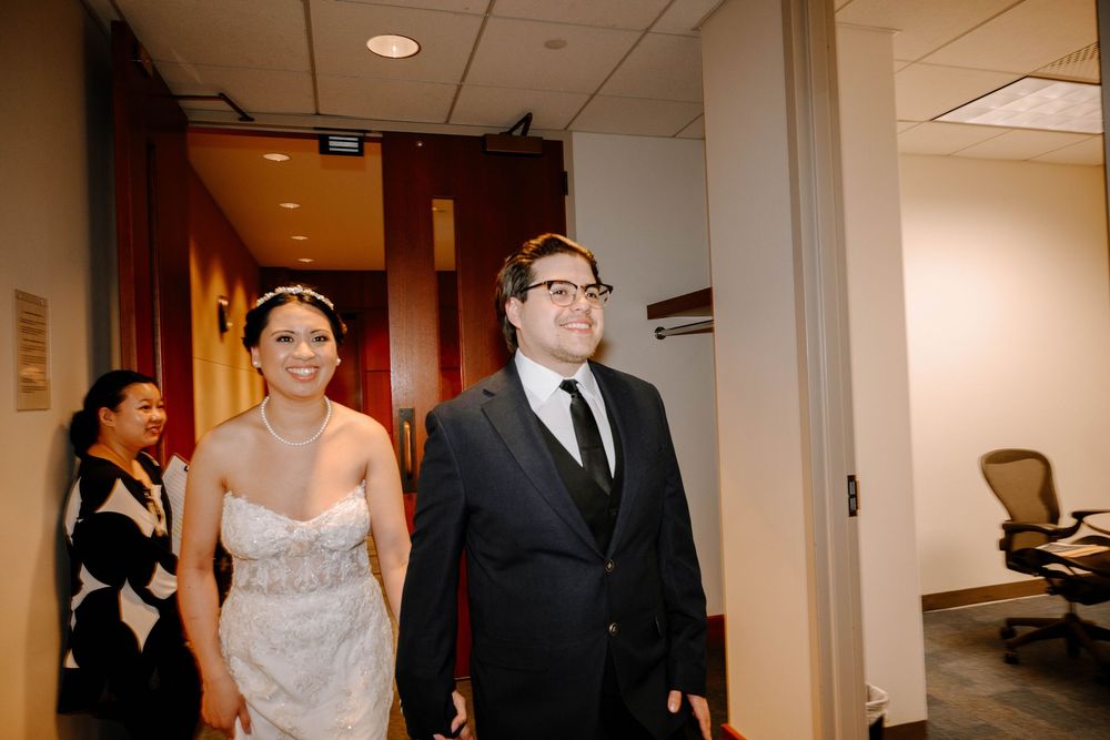 A couple walks down a bright office hallway while followed by another person in formal attire.