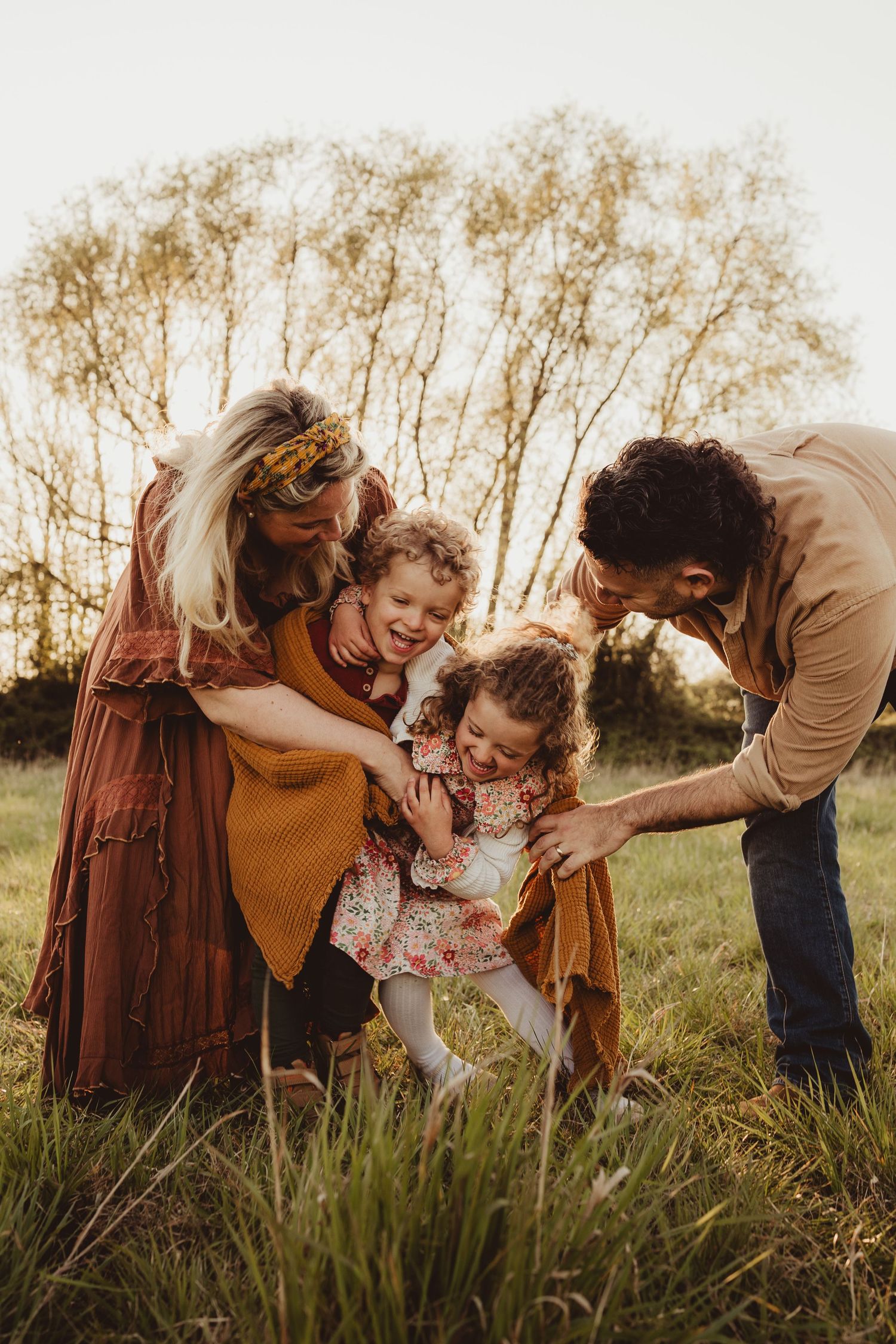 A family plays and laughs together in a golden field at sunset while dressed in warm autumn colors.