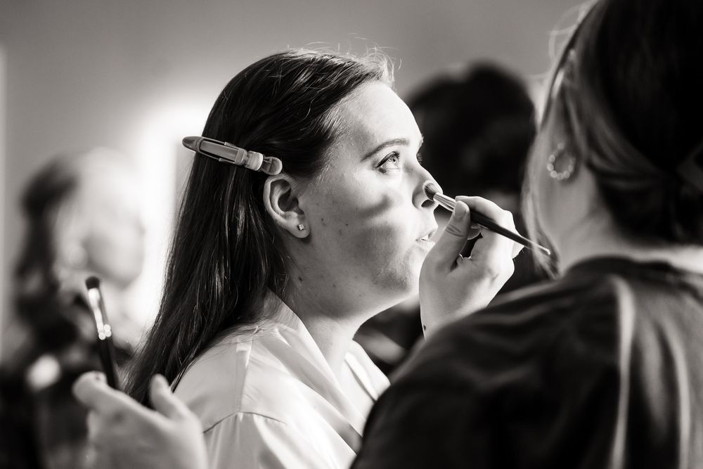 Black and white photo of makeup application during wedding preparations.