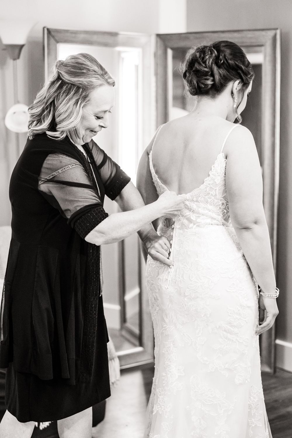 Helper adjusting elegant lace wedding dress straps on a bride during preparations.