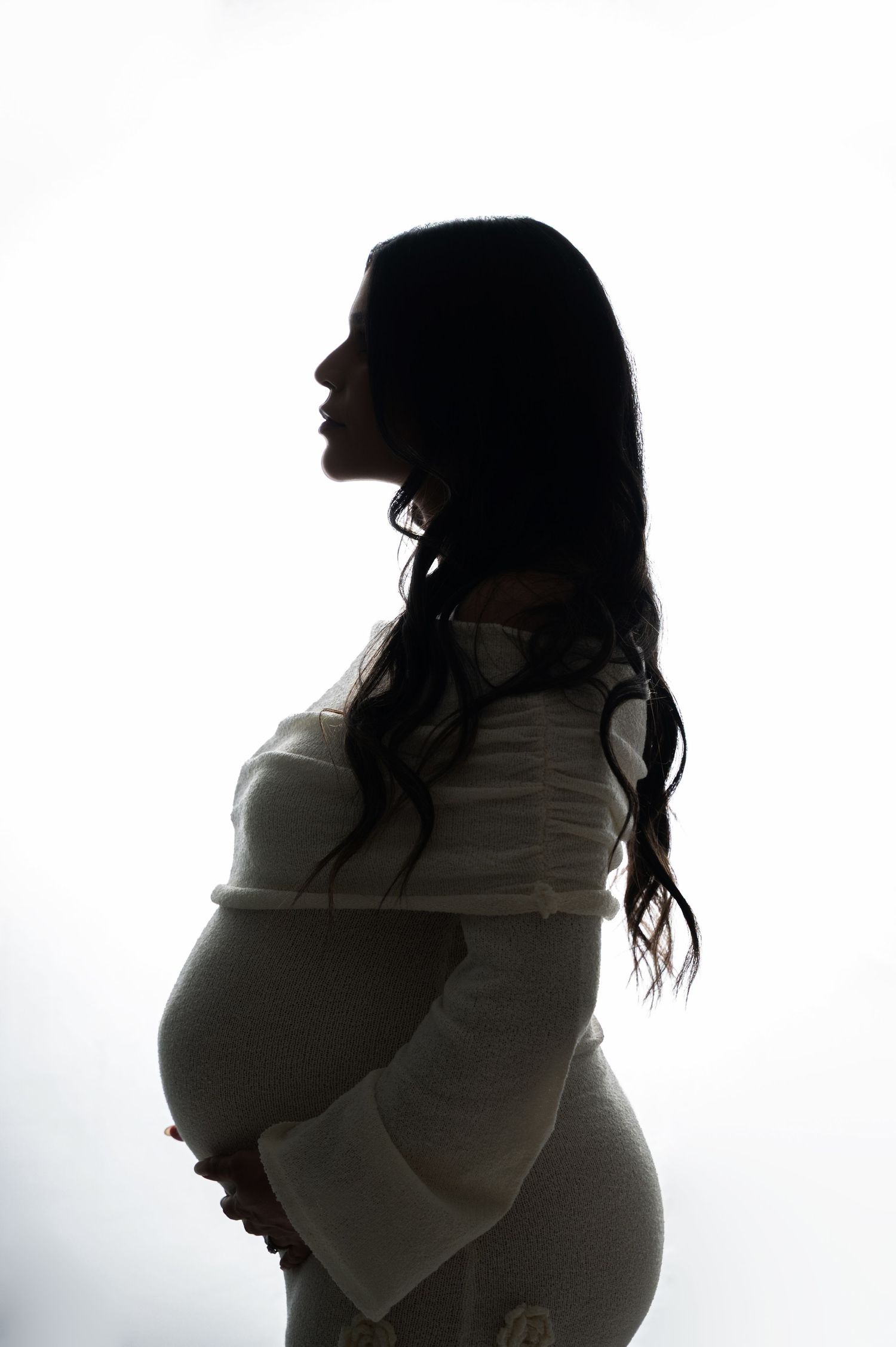 A silhouetted profile of a pregnant woman in a white dress stands against a bright background.