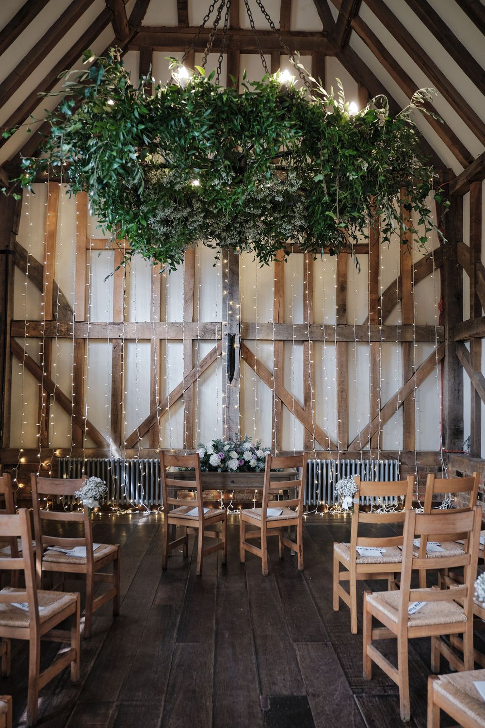 Rustic barn wedding venue with wooden chairs and elegant greenery chandelier hanging from exposed timber beams.