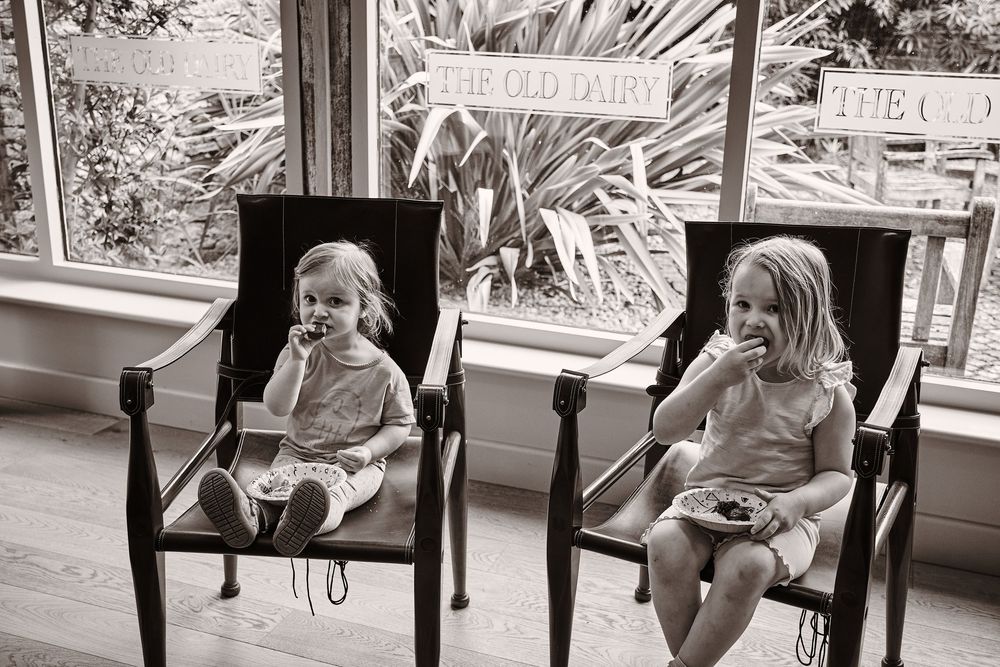 Vintage black and white photograph of two children sitting in wooden chairs by a window.