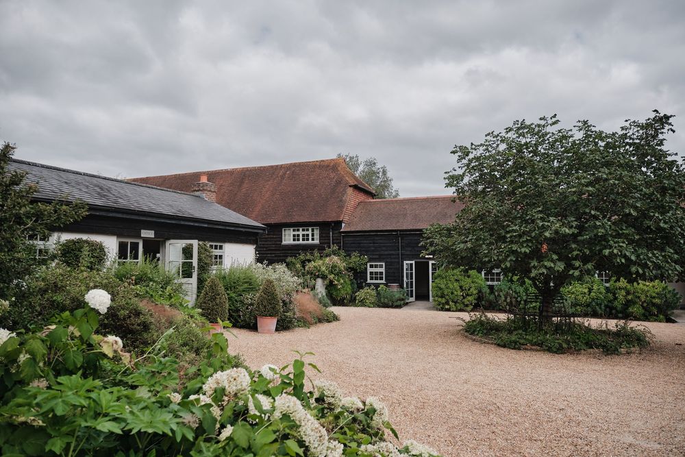Rustic barn-style venue with landscaped gardens and gravel driveway under cloudy skies.