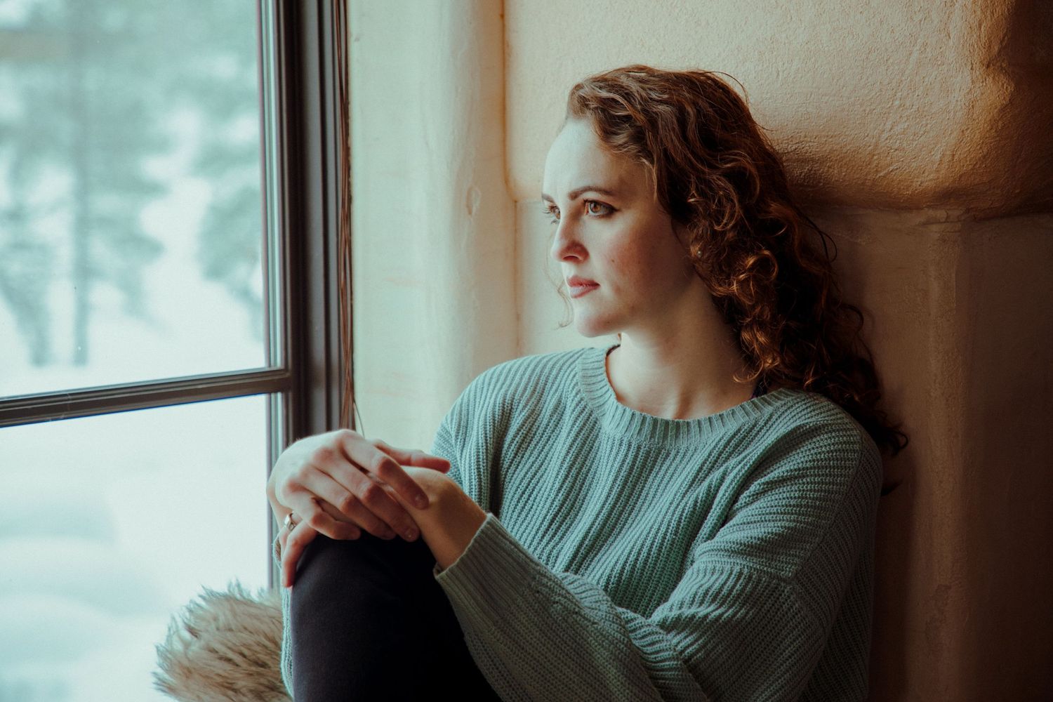 Contemplative scene by a window with soft natural lighting and muted teal tones.