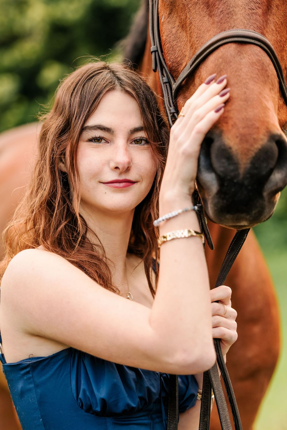 A beautiful chestnut horse nuzzles close to someone in an elegant blue dress outdoors.