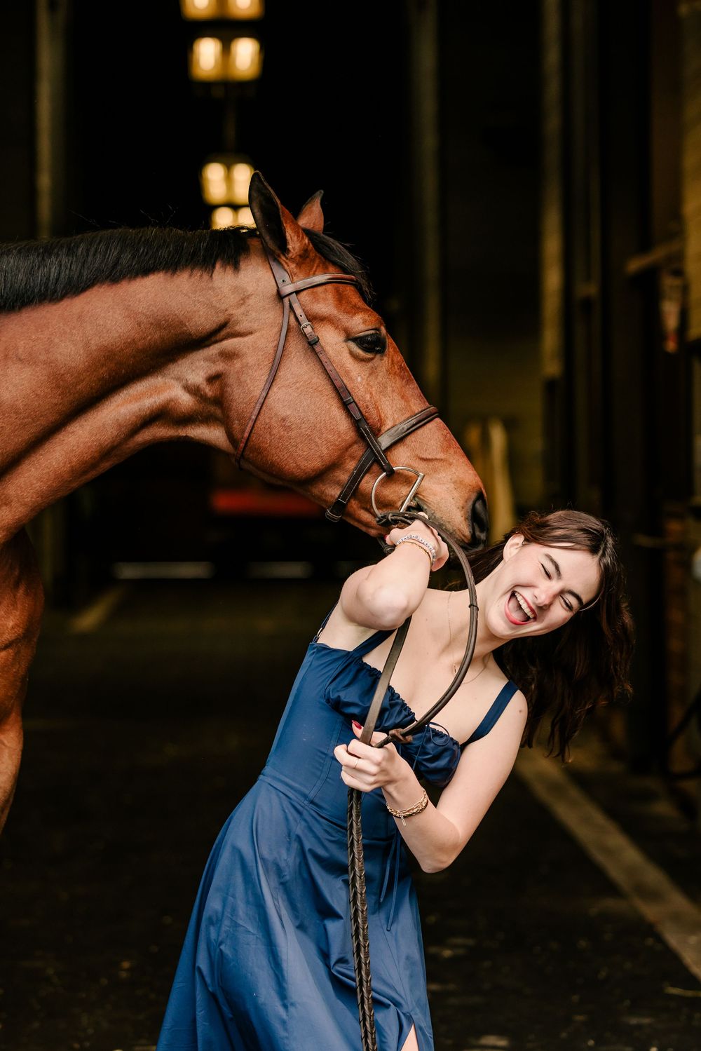 A joyful interaction between a horse and person in a blue dress inside a rustic barn setting.