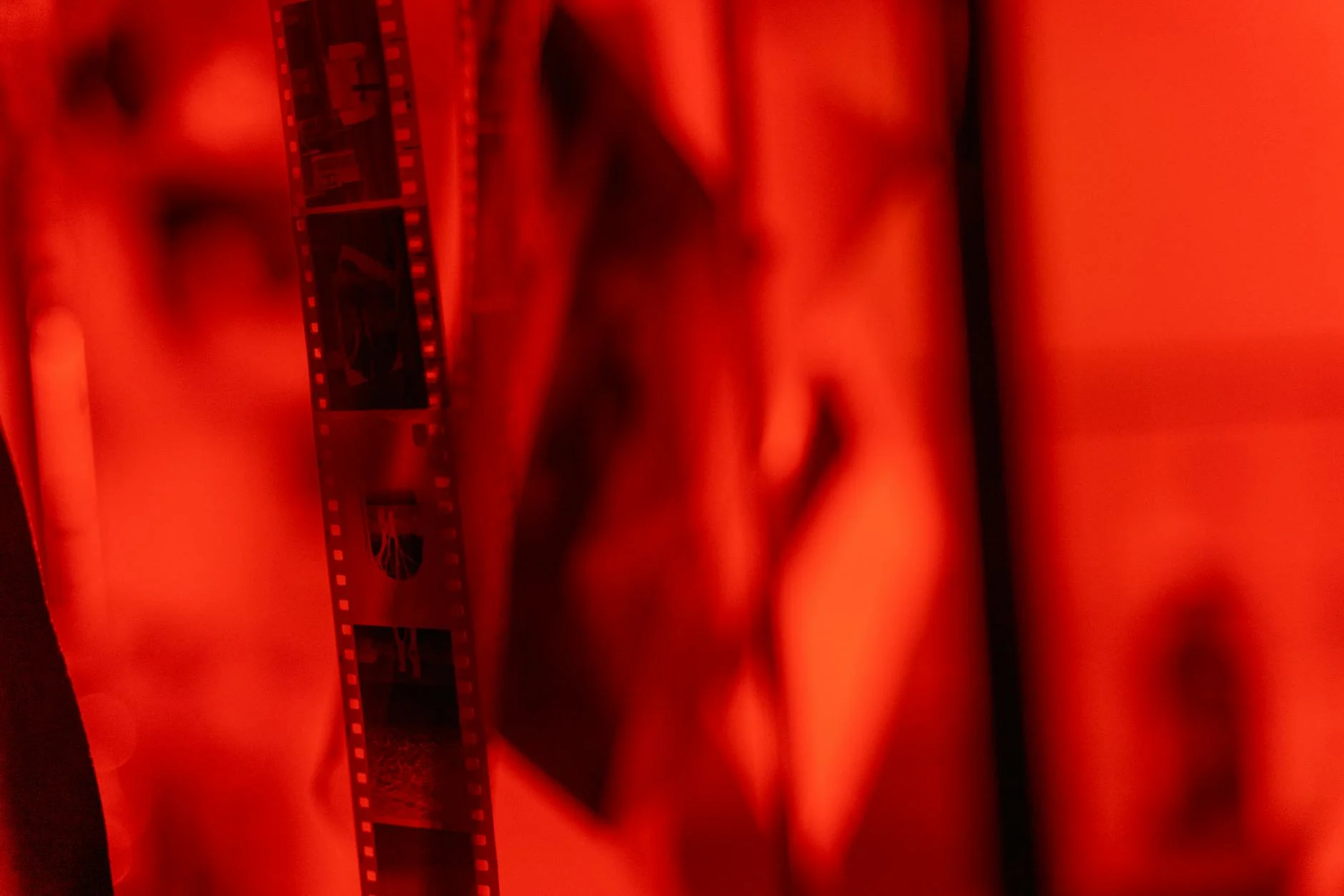 Abstract close-up view of film strip negatives bathed in vibrant red lighting creating a moody atmospheric effect.