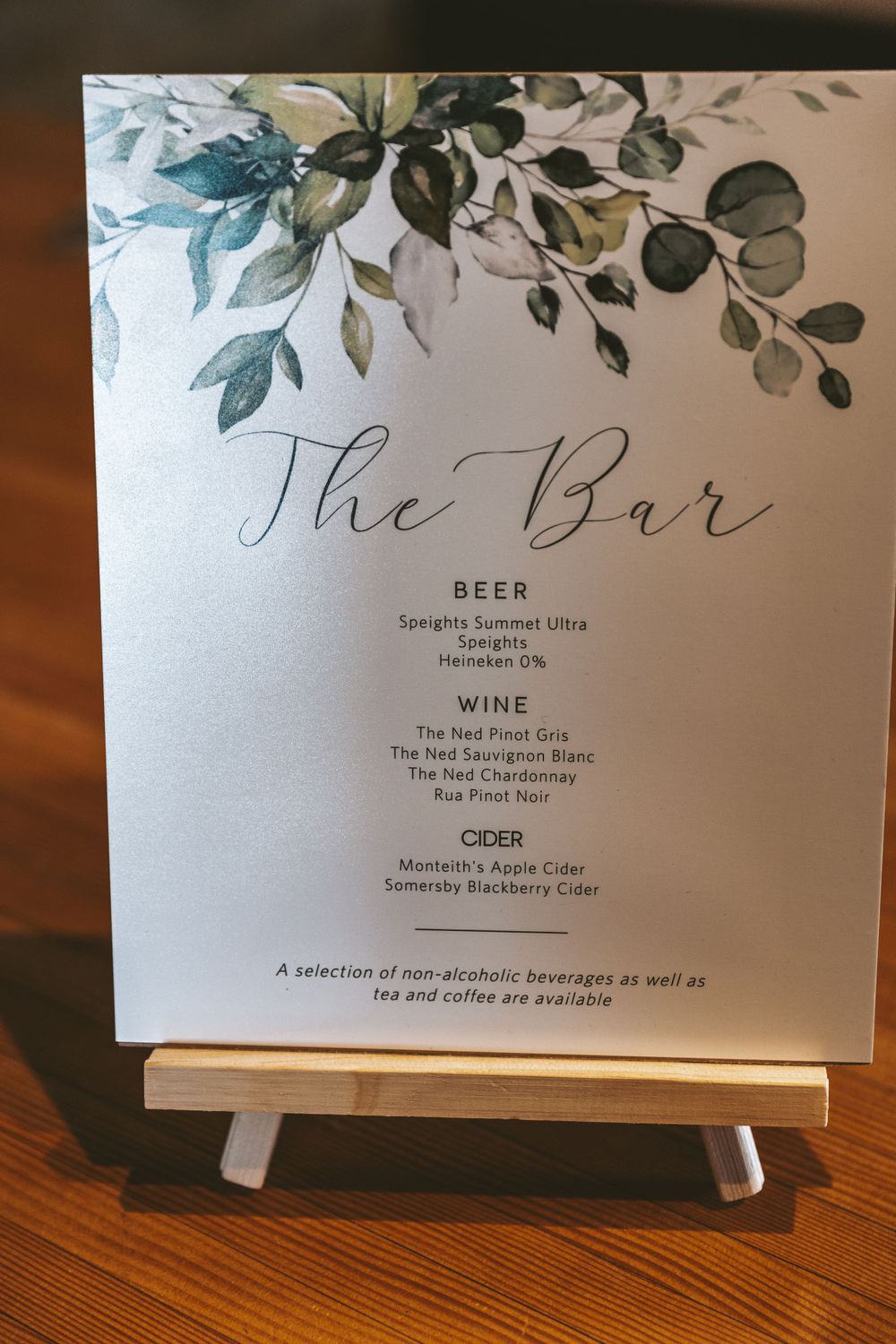 Bar menu sign with elegant greenery design displayed on small easel.