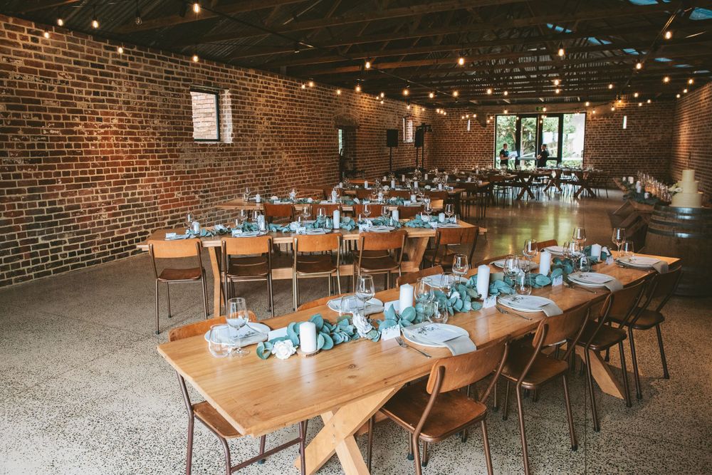 Rustic wedding reception setup with wooden tables and string lights in an industrial brick venue.