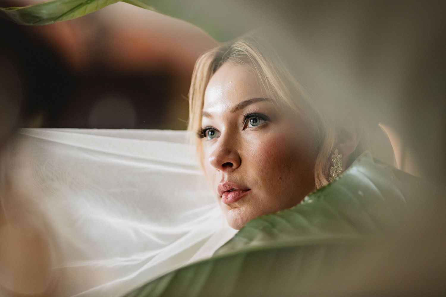 Artistic portrait shot through green leaves with soft natural lighting and dreamy atmosphere.
