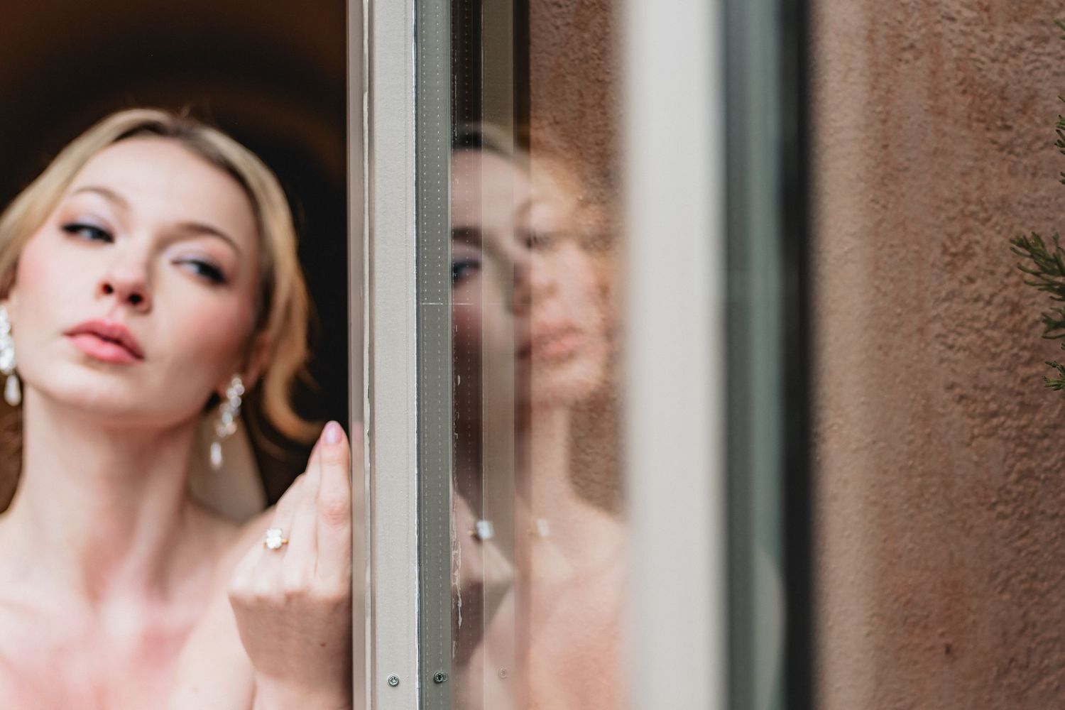 A reflection appears in a window glass against a textured brown wall as light softly illuminates the scene.