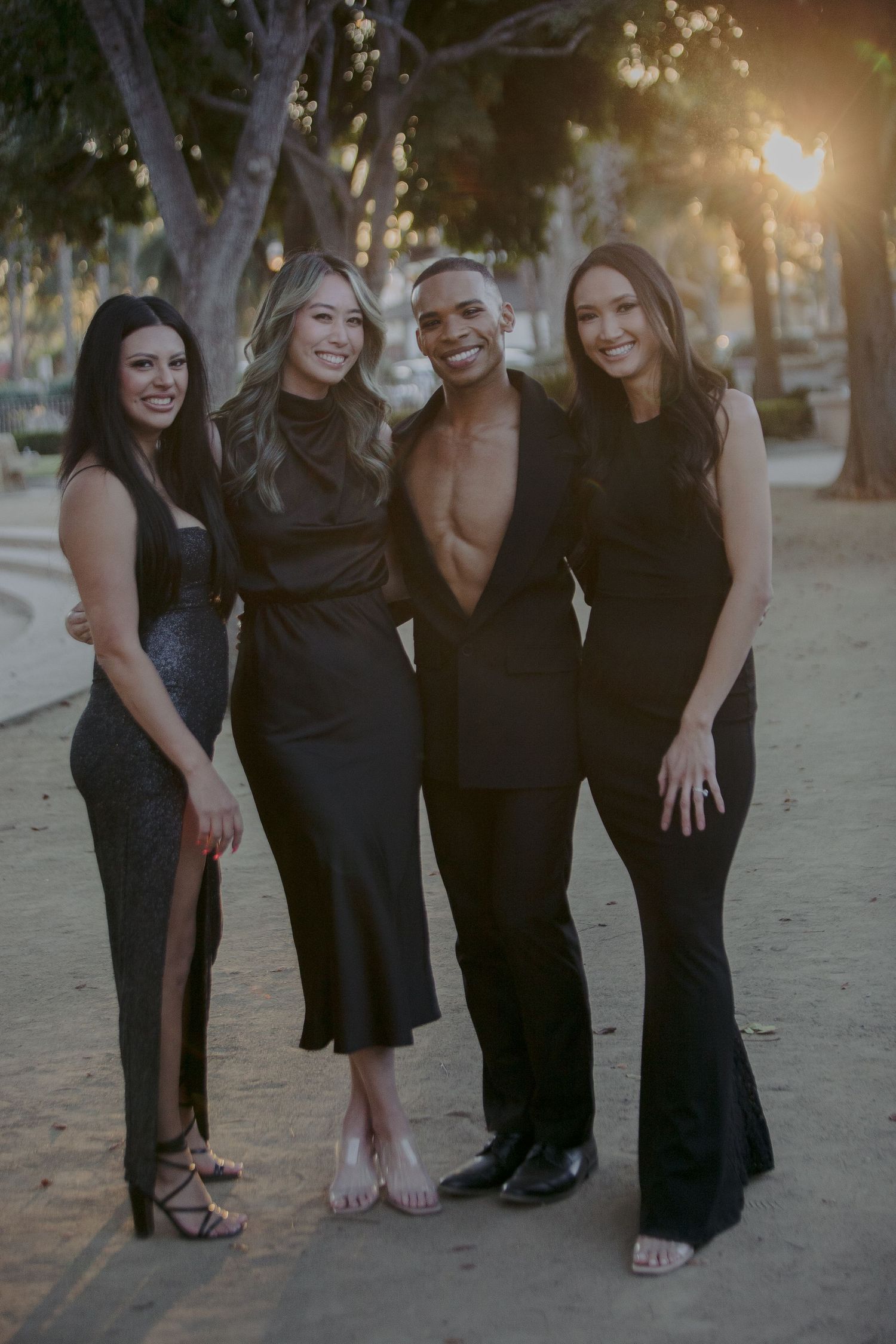 A group poses together outdoors at sunset while wearing formal black attire.