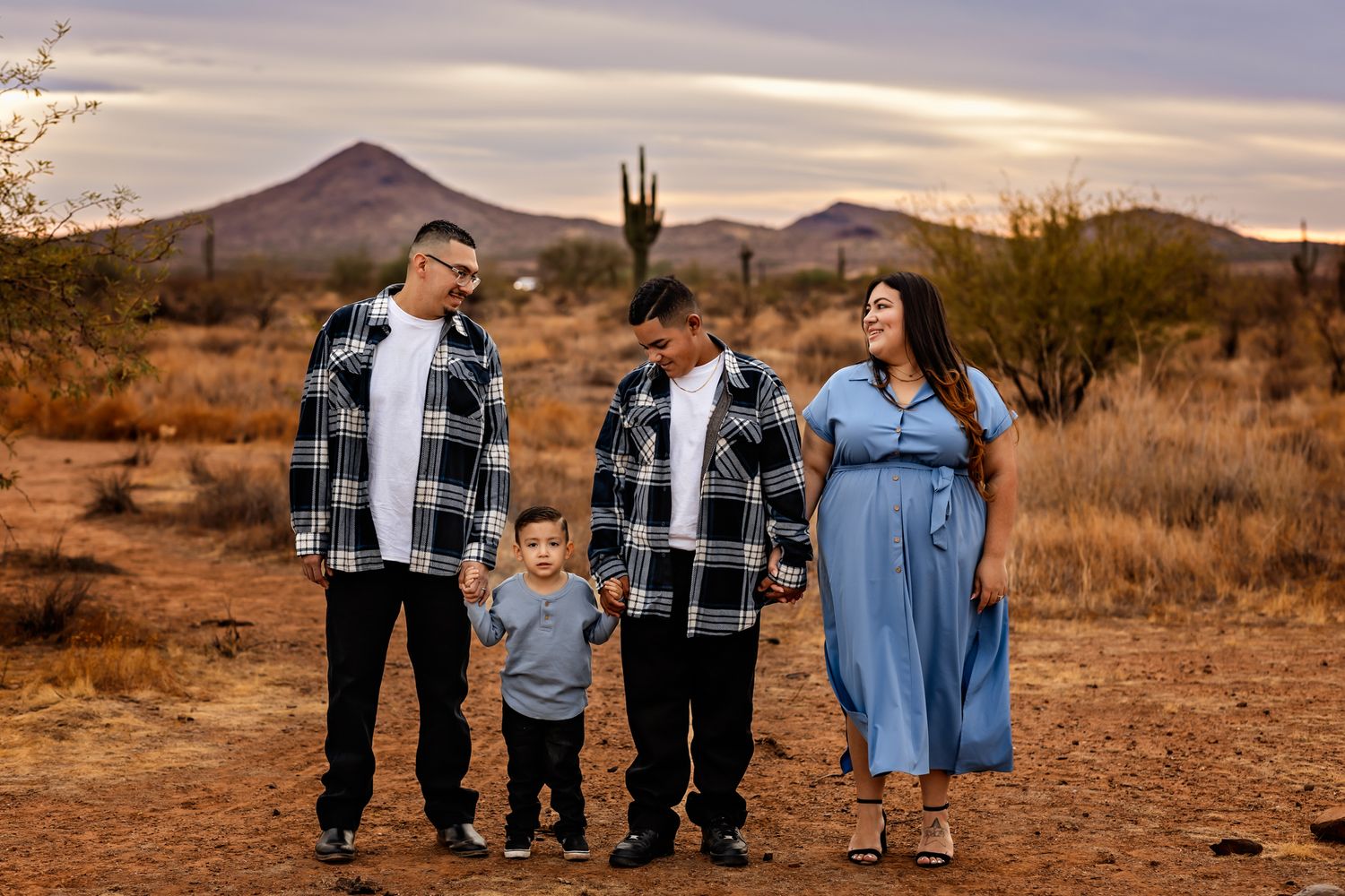 A family stands together in the Arizona desert at dusk with mountains and saguaro cacti in the background.