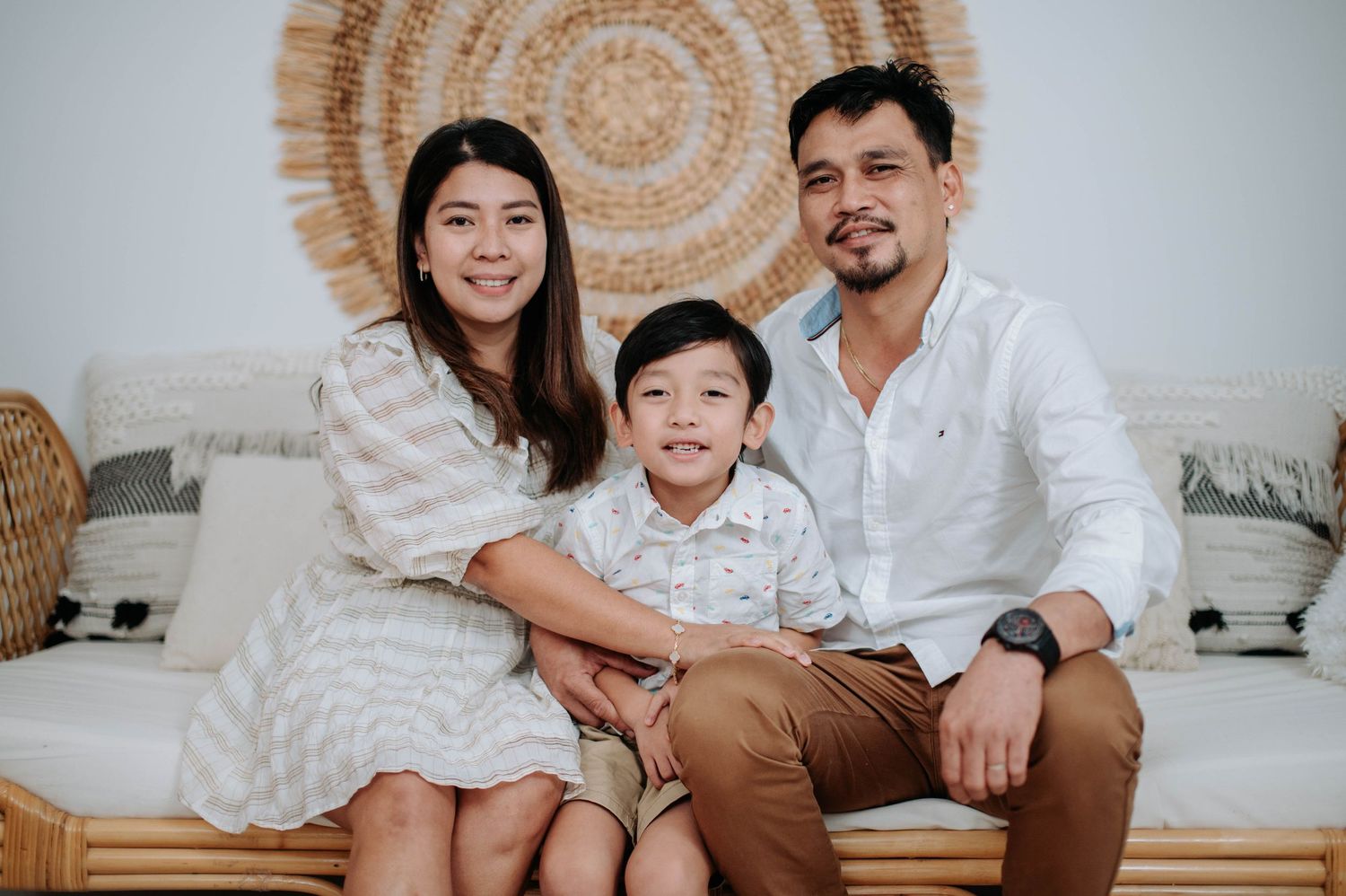 Smiling family in white and beige outfits sitting together on a sofa, sharing joyful moments in a bright living room.