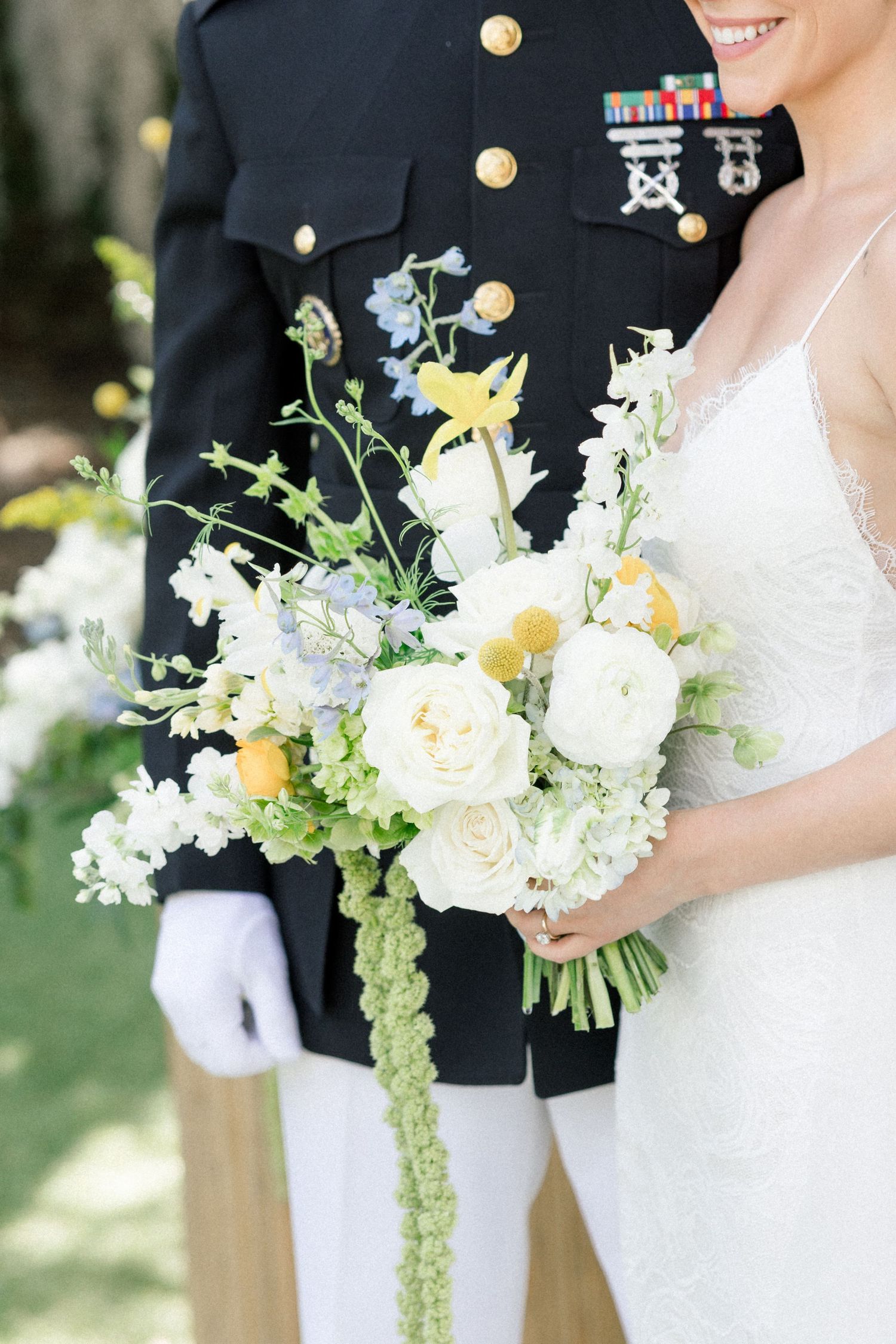 A military wedding bouquet with white roses and yellow flowers next to formal dress uniform with medals.