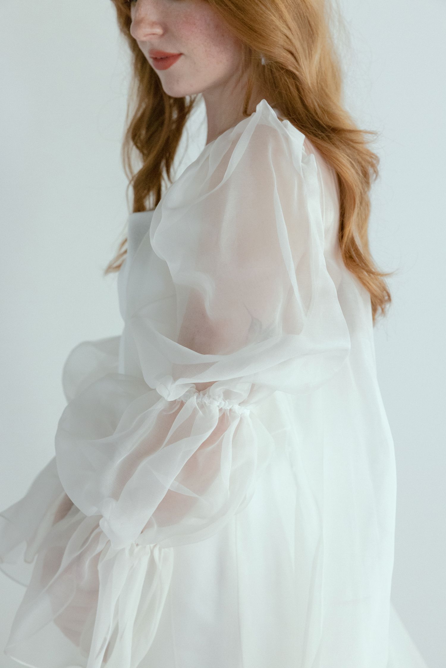 Ethereal white sheer gown with billowing sleeves and delicate details photographed against minimal backdrop.