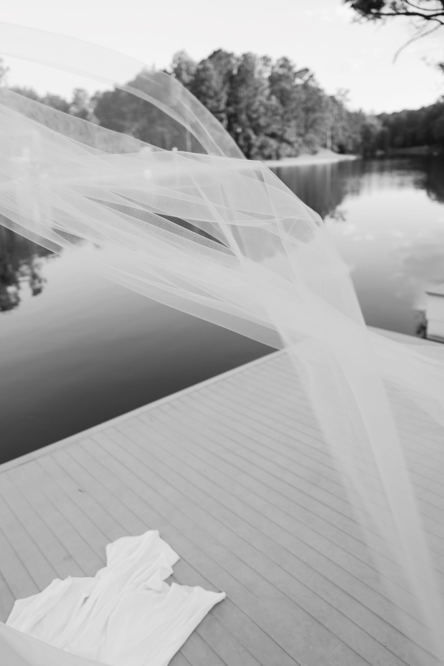 Wedding veil flowing in the breeze on wooden dock by tranquil lake.