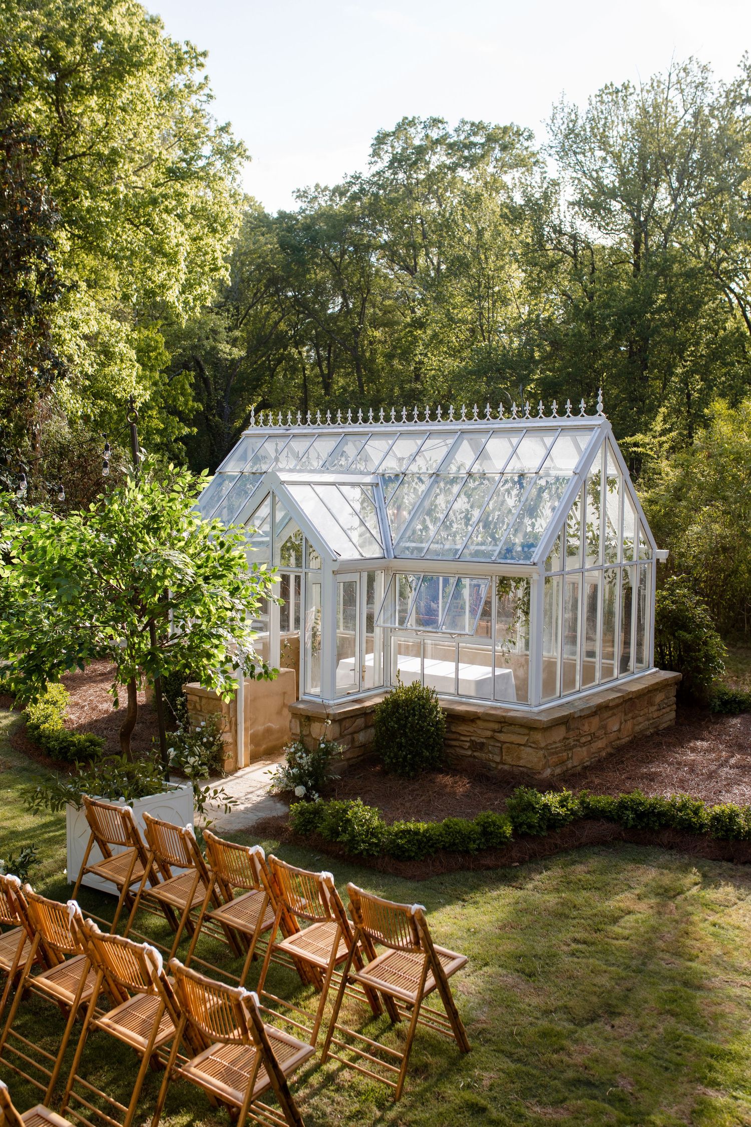 A beautiful greenhouse wedding venue with wooden chairs set up for an outdoor ceremony in a garden setting.