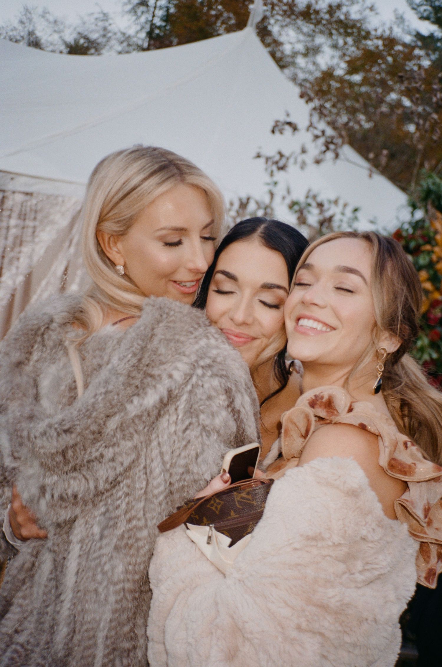 Three people share joyful, tender moments together outdoors against an autumn backdrop.