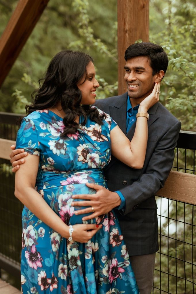 Couple embraces in an outdoor setting while wearing a blue floral dress and dark suit.