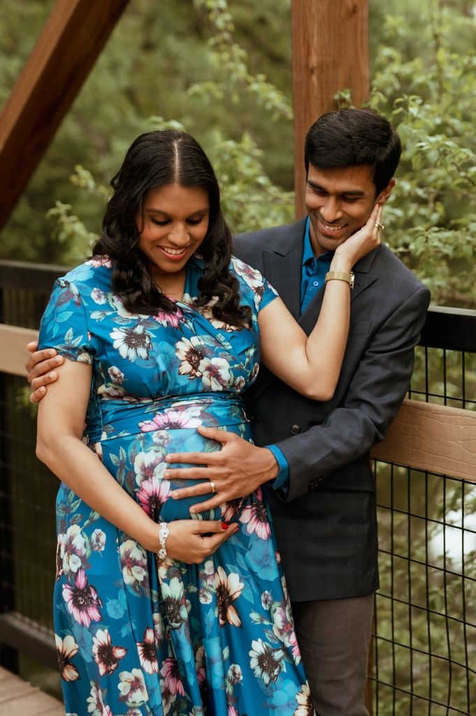 A couple share an intimate moment outdoors as they await their baby, with her wearing a blue floral maternity dress.