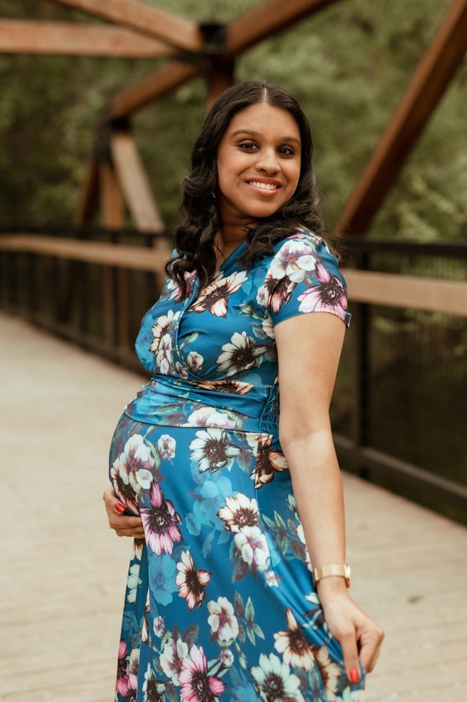 Person in blue floral print dress stands on wooden bridge outdoors in natural setting.