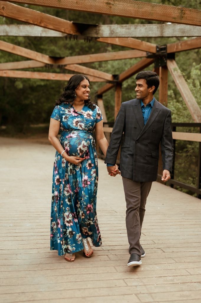 A couple walks hand-in-hand on a wooden bridge in nature, the person in blue dress and person in dark suit.