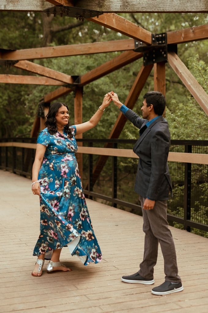 Two people dancing together under a wooden bridge structure as sunlight filters through the beams.