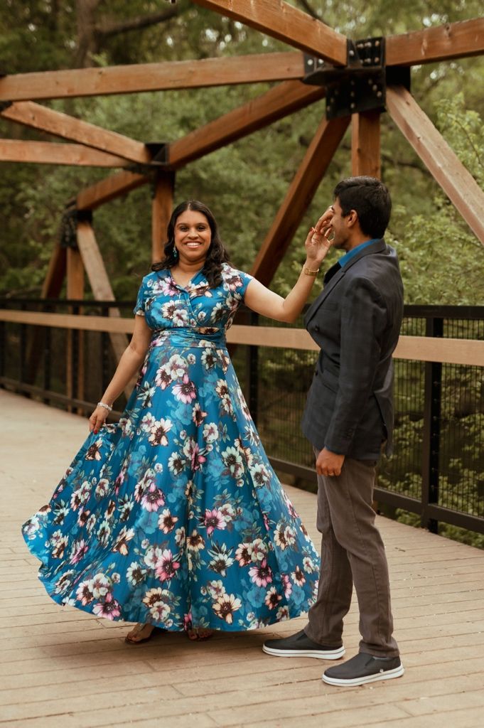 A couple dances together on a wooden bridge, with the woman wearing a flowing blue floral dress.