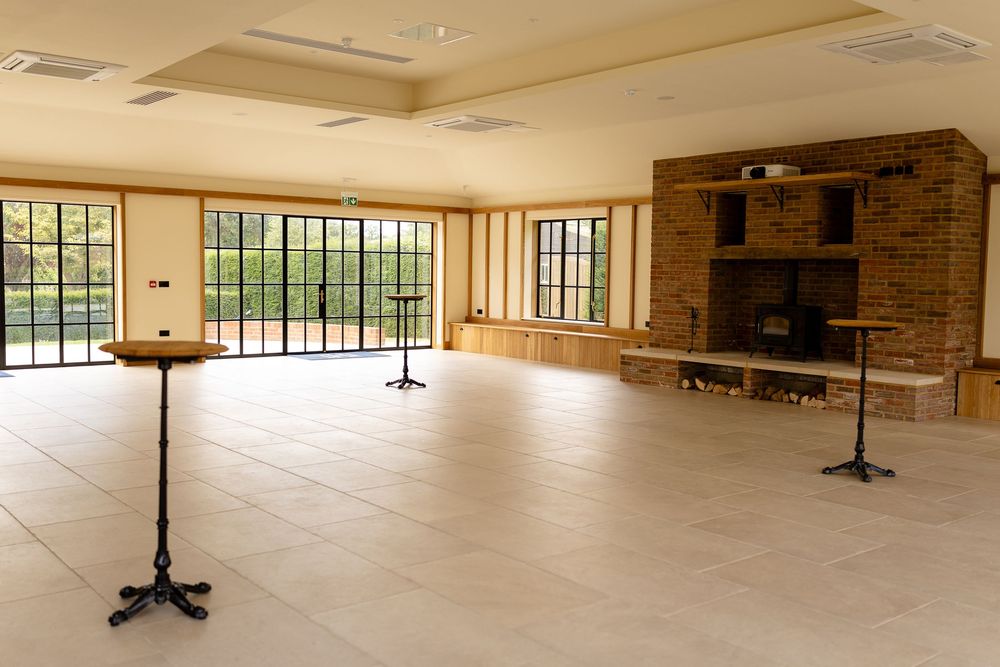 Large empty dance studio with brick fireplace, floor-to-ceiling windows, and wooden coat stands.