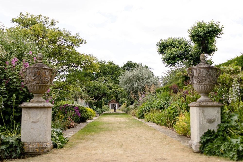 A stone-lined garden path leads through lush greenery and flowering plants to a distant viewpoint.