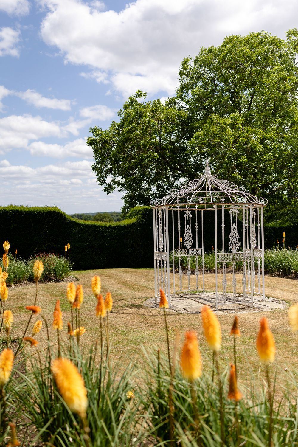 Metal gazebo structures stand in a garden with orange torch-like flowers blooming in the foreground.